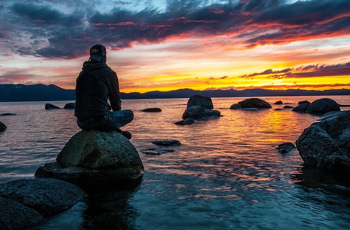 Um homem ao pôr do sol sentado em uma pedra na praia, expressando serenidade